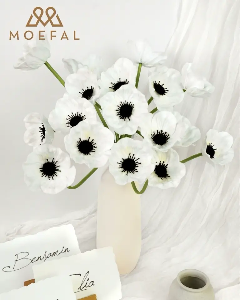 White anemone bouquet in a slender vase sits on a draped table with calligraphy cards.