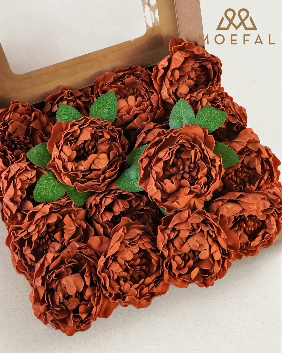 An open box full of burnt orange artificial terracotta peonies with green leaves.