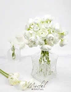 A beautiful bundle of white bud vase ranunculus in a vintage clear glass vase.