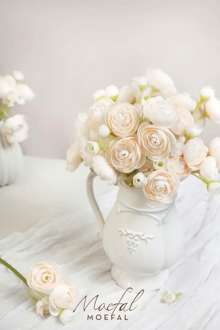 A lush bouquet of artificial cream ranunculus arranged in a white vintage style pitcher.