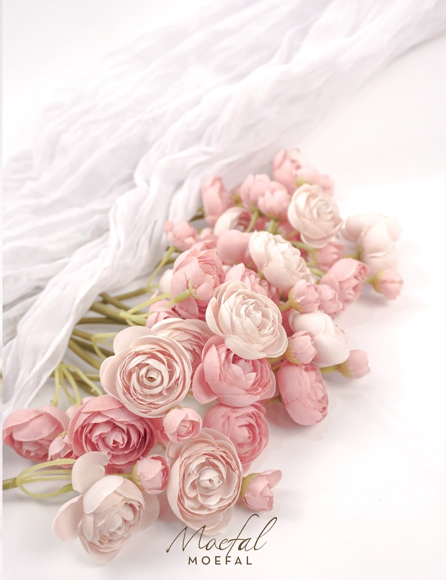 A bundle of dusty rose ranunculus stems laid beautifully beside a draped white cloth.