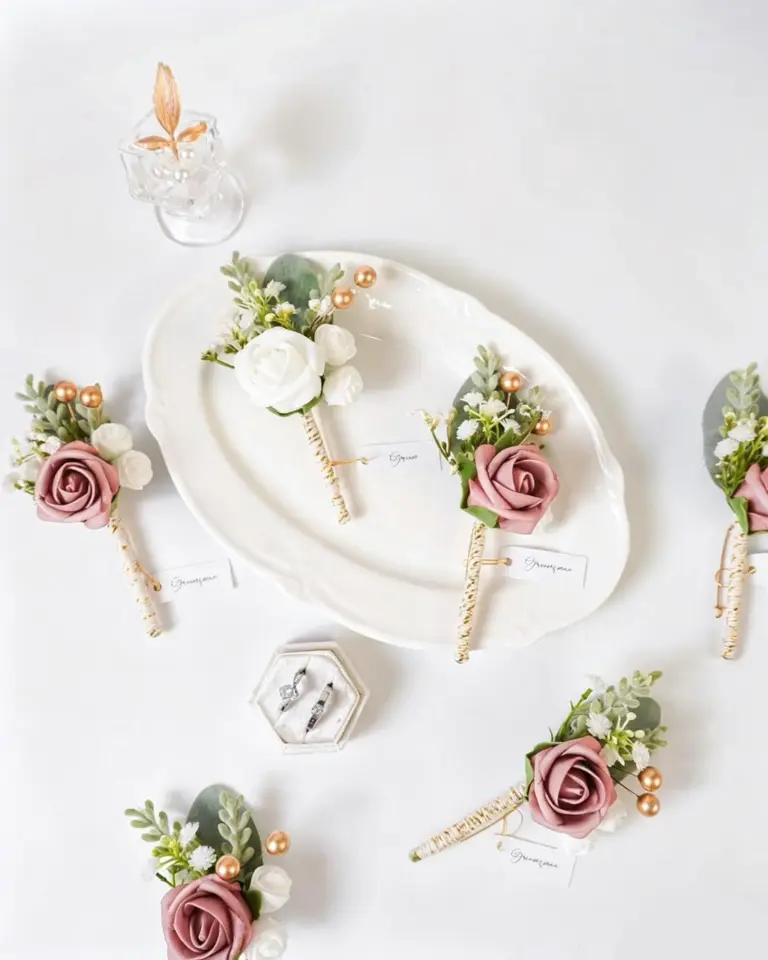 A collection of dusty rose and ivory pre-made boutonnieres arranged on a white platter.