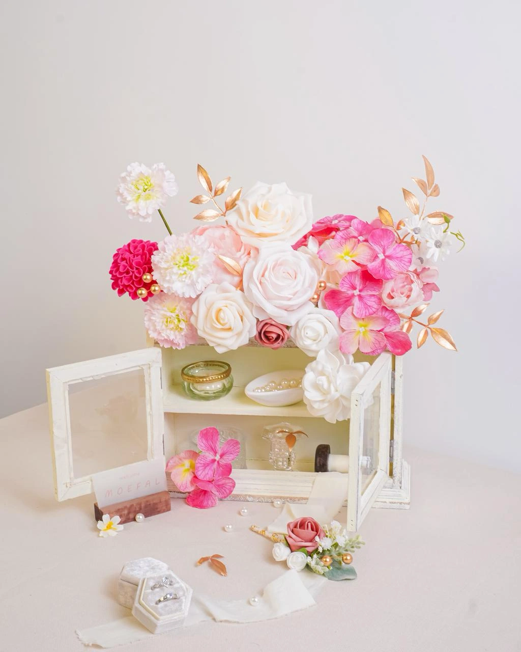 A pink and white bridal bouquet displayed in a shadow box with wedding mementos.