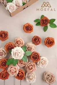 A flat lay of terracotta color palette foam roses scattered on a beige fabric.