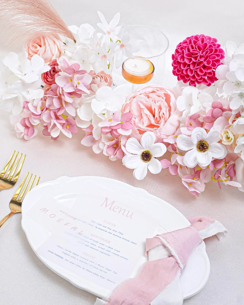 A romantic place setting with a lush pink floral garland for a vintage garden wedding.