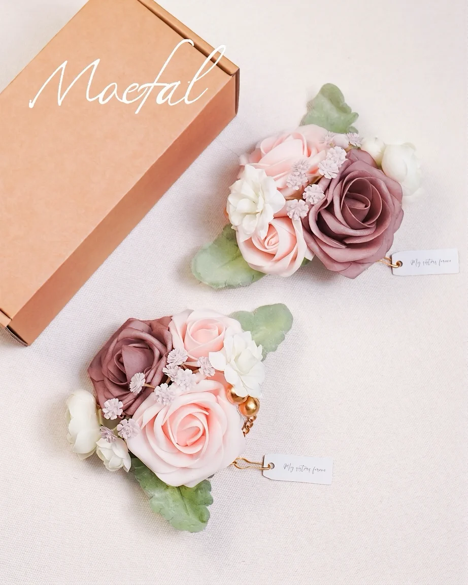 A pair of dusty rose wedding wrist corsages displayed next to a brown gift box.