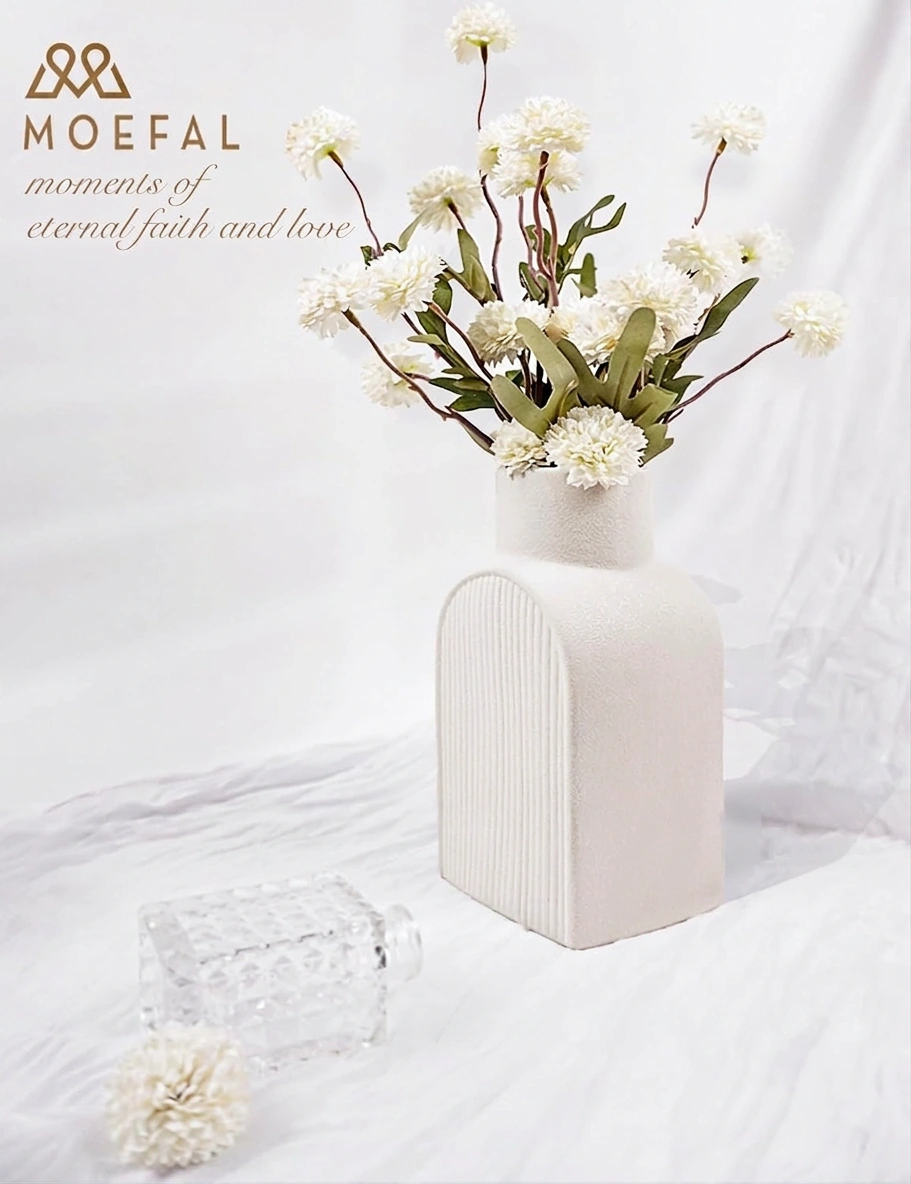 A bouquet of white pompon mums styled in a textured, U-shaped white ceramic vase.